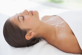 Beautiful brunette lying on massage table with salt scrub on chest at 